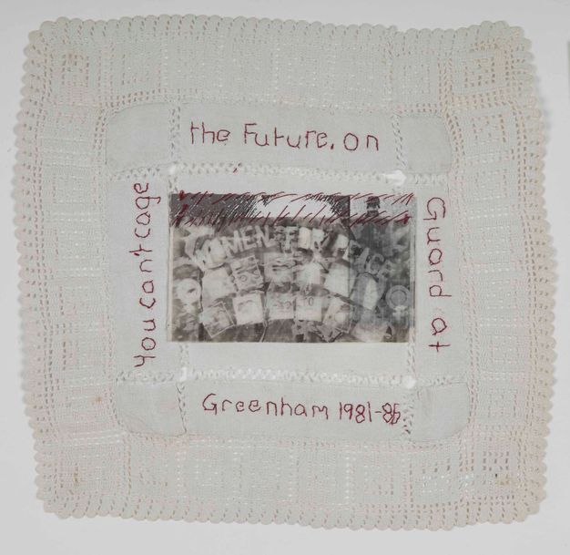 Textile. A black and white image reading 'Women for Peace' is stitched to a square piece of lace. Text also stitched in red around the image reads 'You can't cage the future. On Guard at Greenham 1981-86.