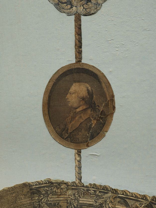 Print. An oval portrait showing a pale-skinned man from the chest up facing our left in profile is affixed to a pale blue wall. Printed ropes above and below connect it to other works, out of view in this detail.